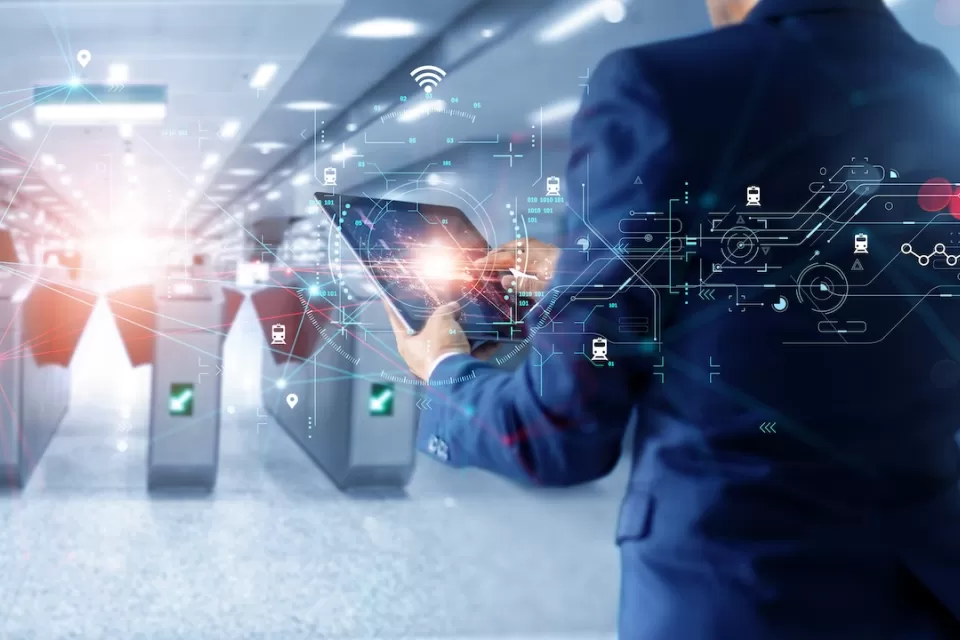 Man in suit holding tablet looking at subway turnstiles with superimposed graphics signaling technology and AI.
